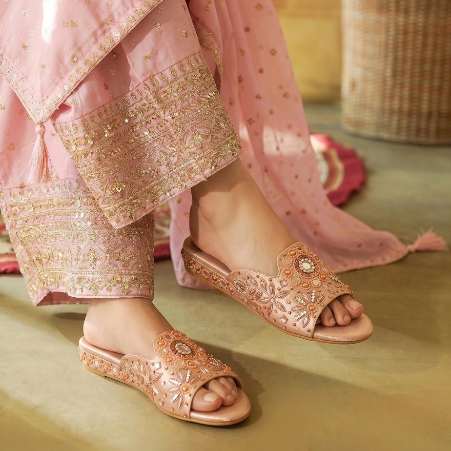 Decorative pink sandals worn with matching traditional outfit on a soft surface.