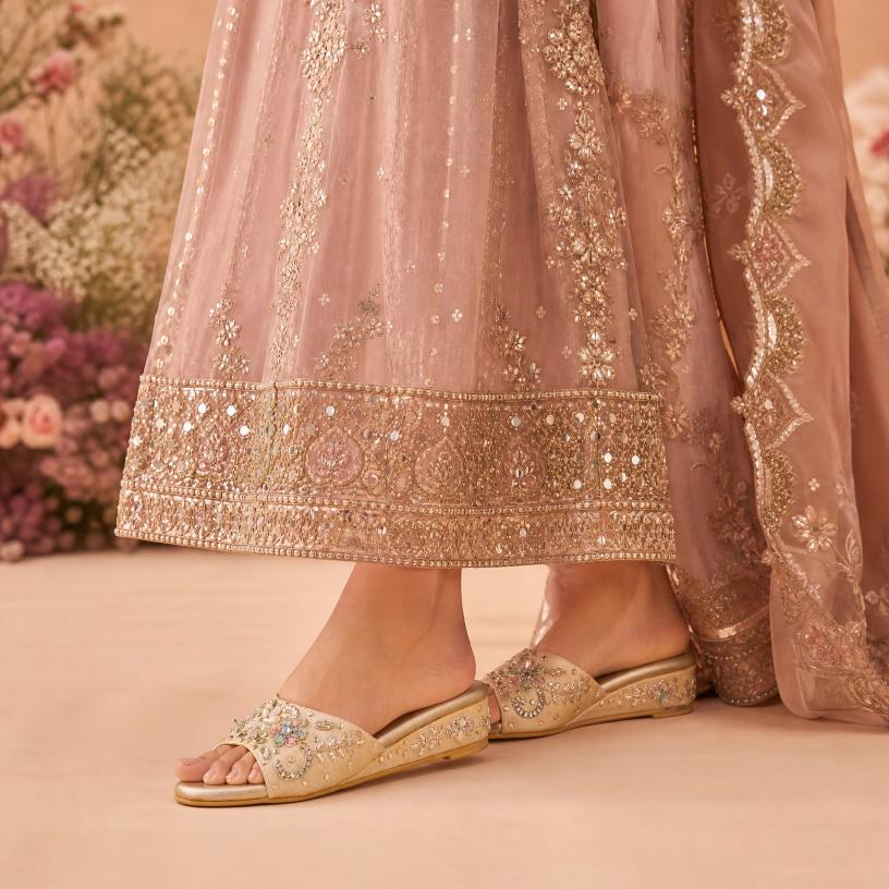 Decorative pink traditional outfit with gold embroidery and matching sandals on a neutral background.